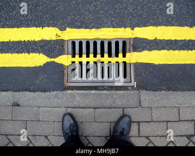 Doppelzimmer mit gelben Linien gehsteig Bürgersteig Füße Schuhe mit Gitter Kanaldeckel über Straße Straße lackiert Stockfoto