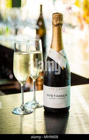 Ungeöffnete Nyestirm-Champagner-Flasche und zwei gefüllte Sektflöten auf einem Tisch, verschwommener Hintergrund. Stockfoto