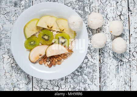 Haferflocken mit Äpfeln, Birnen, Walnüsse und Kiwi in einer weißen Schüssel. Ansicht von oben. Stockfoto