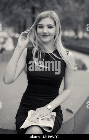 Smart Blonde Mädchen sitzen mit Zeitung und Lesen Stockfoto