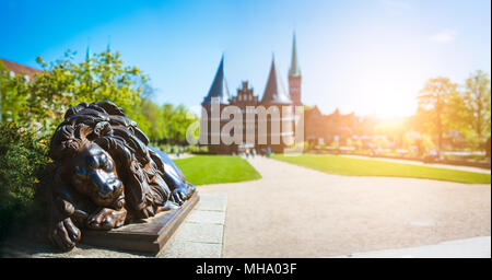 Bronze Lion Statue vor dem Holstentor - Panorama-aufnahme der Holstentor und Park, eine Stadt Tor markieren die westliche Grenze der Altstadt von Lübeck in Schleswig-Holstein Stockfoto