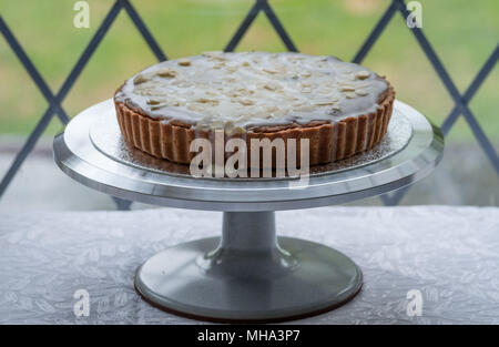 Home gebackene Bakewell Tart Kuchen auf Metall Kuchen stand vor dem Fenster, mit Garten hinter. Stockfoto