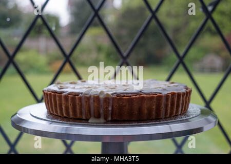 Home gebackene Bakewell Tart Kuchen auf Metall Kuchen stand vor dem Fenster, mit Garten hinter. Stockfoto