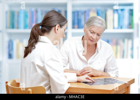 Im mittleren Alter Arzt in Ihrem Büro zeigen Ihr besorgt älterer Patienten die aktuelle MRT des Gehirns Stockfoto