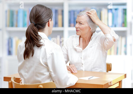 Ältere Frau mit grauen Haaren zeigen Ihr schütteres Haar oder Haarausfall zu Ihrer Ärztin Stockfoto