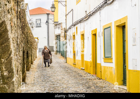 Evora, Portugal - Dezember 9,2017: ältere Frau zu Fuß auf der schmalen Straße zwischen der alten römischen Brücke und traditionelle Häuser Stockfoto