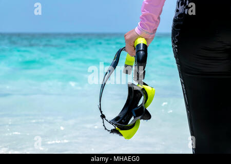 Frau am Strand und Badeanzug rosa. Holding Schutzbrille, Tauchen, Schwarz-gelb. Glückliches Lächeln. Der Hintergrund ist Himmel und Meer. Stockfoto