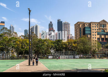 Zwei Frauen bei einem Spaziergang durch den Victoria Park, Hong Kong während einige Jungs Fußball spielen. Die Hochhäuser der Stadt kann im Hintergrund gesehen werden. Stockfoto