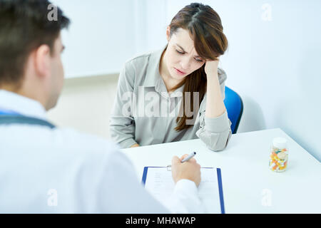 Portrait von stirnrunzelnd junge Frau hören, Arzt beim Sitzen am Schreibtisch, in der Klinik, kopieren Raum Stockfoto