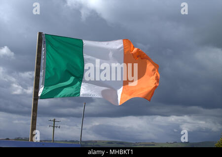 Irland Nationalflagge Tricolour und Stern der Republik Irland fliegen in einem steifen Wind gegen einen stürmischen Himmel. Stockfoto