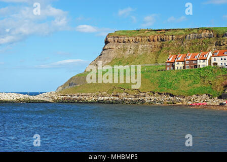 Eine grasbedeckte Landspitze unter einem blauen Himmel über den Fluss Esk von Whitby Stadt gesehen, mit einer Reihe von roten Dächern auf der Landzunge von Stockfoto