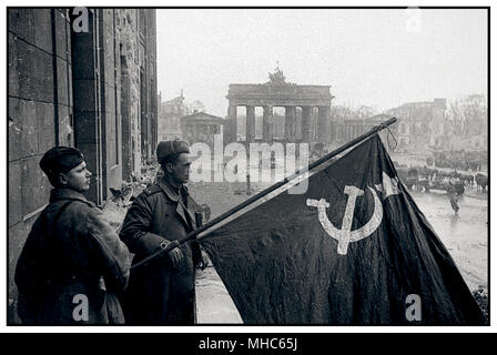 1945 russische Soldaten halten stolz ihr Nationalsymbol Hammer und Sichelflagge im Sieg Berlin Deutschland das Brandenburger Tor liegt in einem sehr schroffen und zerschlagenen Zustand dahinter. Einst ein Symbol des deutschen Stolzes, liegt es hier im Mai 1945 fast in Ruinen, nachdem es von den Alliierten bombardiert und von den Besatzungsrussen geschlagen wurde Stockfoto