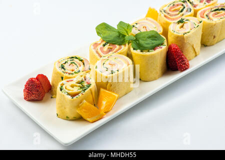 Rollen von dünnen Pfannkuchen mit geräuchertem Lachs, Meerrettich Frischkäse und Rucola Blätter auf weiße Platte auf weißem Hintergrund Stockfoto