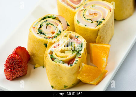 Rollen von dünnen Pfannkuchen mit geräuchertem Lachs, Meerrettich Frischkäse und Rucola Blätter auf weiße Platte auf weißem Hintergrund Stockfoto