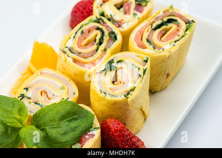 Rollen von dünnen Pfannkuchen mit geräuchertem Lachs, Meerrettich Frischkäse und Rucola Blätter auf weiße Platte auf weißem Hintergrund Stockfoto