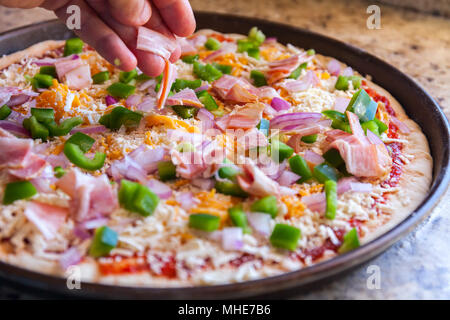 Die Pizza. Cook's Hand streusel Speck und Paprika. Im amerikanischen Stil, kochen in einer Auflaufform Stockfoto