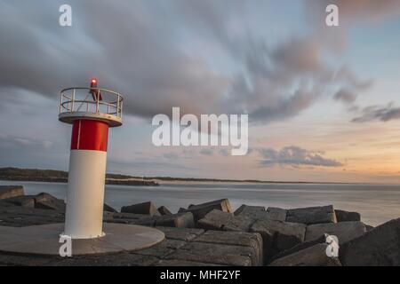 Orange und magenta-farbene sunrise mit der Sonne peeking über dem Horizont. Light Tower im Vordergrund und leichte Cloud Bewegung verwischen. Stockfoto