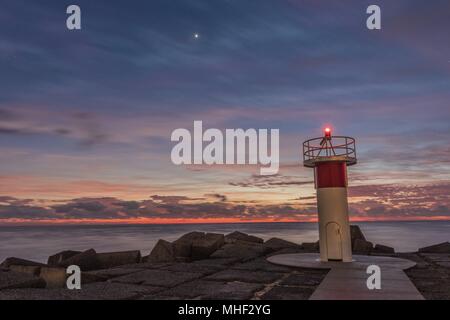 Orange und magenta-farbene sunrise mit der Sonne peeking über dem Horizont. Light Tower im Vordergrund und leichte Cloud Bewegung verwischen. Stockfoto