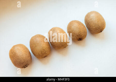 Ganze fünf Kiwis liegen schräg auf einem weißen Tisch Stockfoto