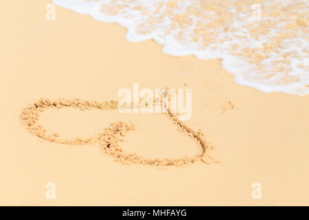 Herzform am Sandstrand vor Wellen waschen Sie es heraus Stockfoto