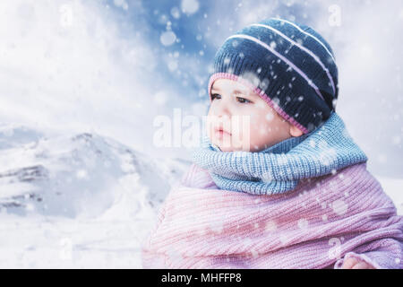 Cute Baby Mädchen mit einem warmen Winter Hut und einem bunten Hut auf einem verschneiten Hintergrund Stockfoto