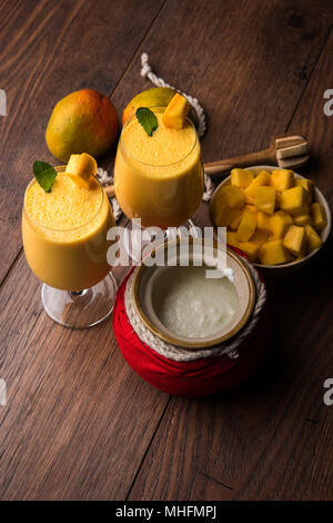 Mango Lassi oder Smoothie in großen Glas oder kleine Flaschen mit Quark, Obst Stücke schneiden und Mixer. Moody Hintergrund, selektiver Fokus Stockfoto