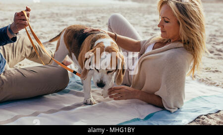 Ältere Frau am Strand Handtuch mit Hund und ihr Mann. Reifes Paar entspannende mit Haustier Welpen am Ufer. Stockfoto