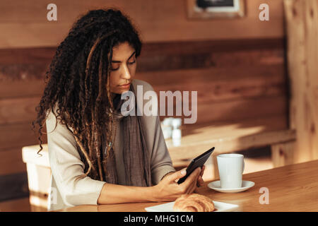 Frau sitzt in einem Restaurant können Sie über Ihr Mobiltelefon. Frau sitzt in einem Café mit Kaffee und Snacks auf den Tisch. Stockfoto