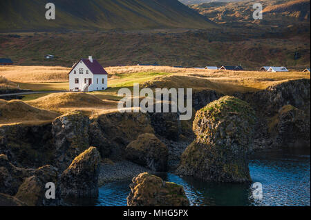 Haus in hügeliger Landschaft bei Sonnenuntergang in der Nähe des Meeres in Island Stockfoto