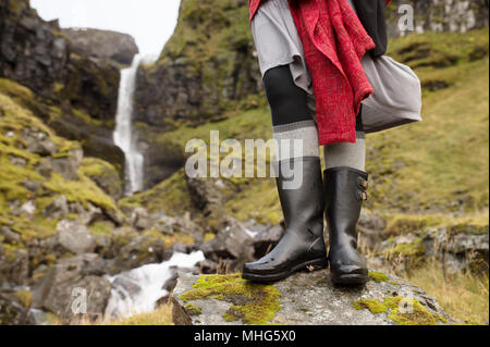 Nahaufnahme der Frau in schwarzer Regen Stiefel vor der isländische Wasserfall Stockfoto