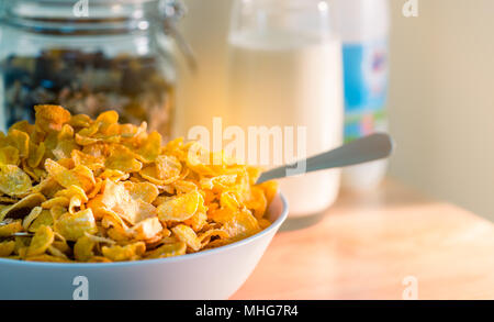 Schüssel Müsli mit Löffel auf Holz Tisch in der Nähe Müsli in Glas Behälter legen und ein Glas Milch. Calcium essen Frühstück für Kinder, bevor sie auf sc Stockfoto