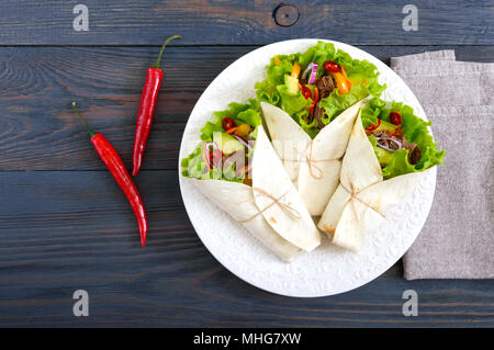 Burrito mit gehacktem Fleisch, Avocado, Gemüse, Paprika, auf einem Schild auf einem dunklen Hintergrund. Gefüllte Tortilla. Traditionelle mexikanische Vorspeise. Zu Stockfoto