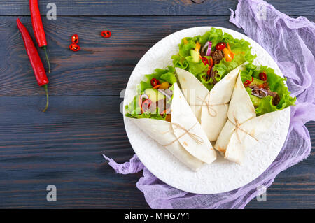 Burrito mit gehacktem Fleisch, Avocado, Gemüse, Paprika, auf einem Schild auf einem dunklen Hintergrund. Gefüllte Tortilla. Traditionelle mexikanische Vorspeise. Zu Stockfoto