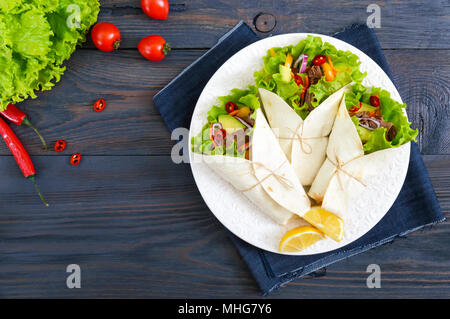 Burrito mit gehacktem Fleisch, Avocado, Gemüse, Paprika, auf einem Schild auf einem dunklen Hintergrund. Gefüllte Tortilla. Traditionelle mexikanische Vorspeise. Zu Stockfoto