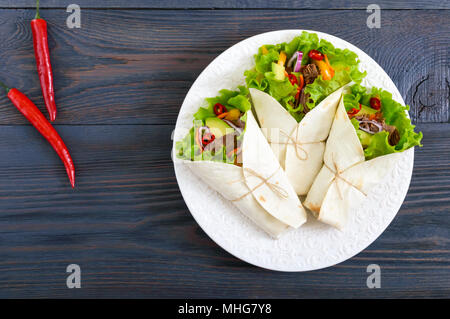 Burrito mit gehacktem Fleisch, Avocado, Gemüse, Paprika, auf einem Schild auf einem dunklen Hintergrund. Gefüllte Tortilla. Traditionelle mexikanische Vorspeise. Zu Stockfoto