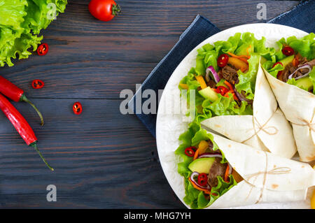 Burrito mit gehacktem Fleisch, Avocado, Gemüse, Paprika, auf einem Schild auf einem dunklen Hintergrund. Gefüllte Tortilla. Traditionelle mexikanische Vorspeise. Zu Stockfoto