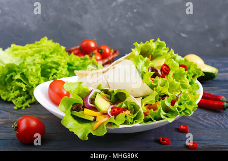 Burrito mit gehacktem Fleisch, Avocado, Gemüse, Paprika, auf einem Schild auf einem dunklen Hintergrund. Gefüllte Tortilla. Traditionelle mexikanische Vorspeise. Stockfoto