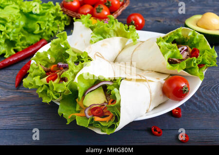 Burrito mit gehacktem Fleisch, Avocado, Gemüse, Paprika, auf einem Schild auf einem dunklen Hintergrund. Gefüllte Tortilla. Traditionelle mexikanische Vorspeise. Stockfoto