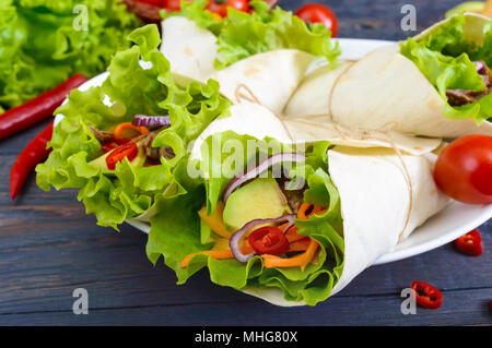 Burrito mit gehacktem Fleisch, Avocado, Gemüse, Paprika, auf einem Schild auf einem dunklen Hintergrund. Gefüllte Tortilla. Traditionelle mexikanische Vorspeise. Stockfoto