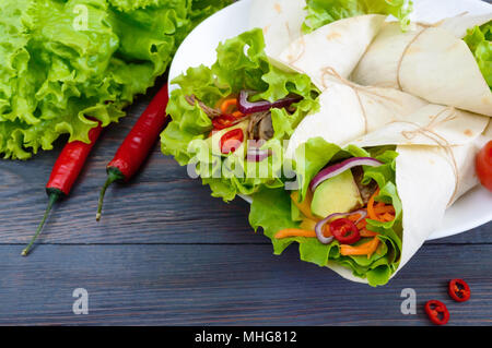 Burrito mit gehacktem Fleisch, Avocado, Gemüse, Paprika, auf einem Schild auf einem dunklen Hintergrund. Gefüllte Tortilla. Traditionelle mexikanische Vorspeise. Stockfoto