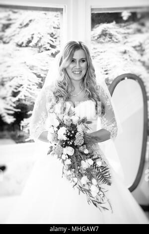 Braut stehen im Fenster. Hochzeit Tag der Vorbereitung. Braut bereit, Kirche, die Hochzeit Blumenstrauß zu gehen und lächelnd. Stockfoto