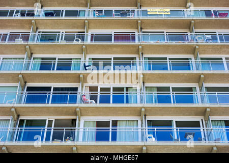 Mann im Sessel ruht auf dem Balkon der Wohnung in Appartementhaus Stockfoto