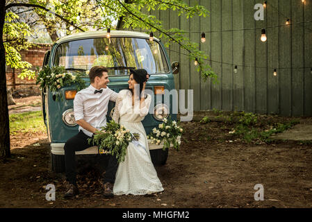 Fröhliches glückliches junges Paar sitzen auf den Stoßfänger retro-Kleinbus. Stockfoto