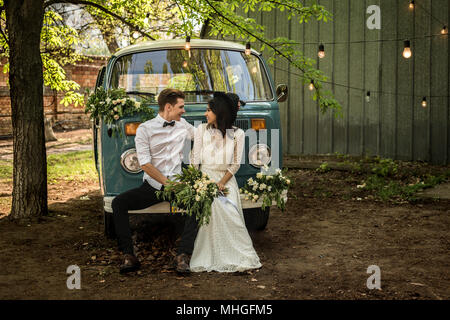 Fröhliches glückliches junges Paar sitzen auf den Stoßfänger retro-Kleinbus. Stockfoto