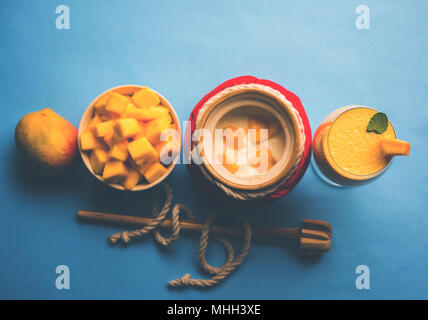 Mango Lassi oder Smoothie in großen Glas oder kleine Flaschen mit Quark, Obst Stücke schneiden und Mixer. Moody Hintergrund, selektiver Fokus Stockfoto