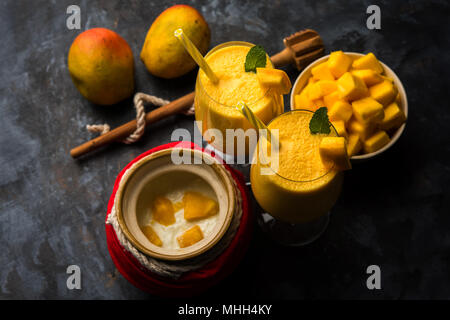 Mango Lassi oder Smoothie in großen Glas oder kleine Flaschen mit Quark, Obst Stücke schneiden und Mixer. Moody Hintergrund, selektiver Fokus Stockfoto