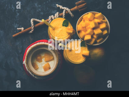 Mango Lassi oder Smoothie in großen Glas oder kleine Flaschen mit Quark, Obst Stücke schneiden und Mixer. Moody Hintergrund, selektiver Fokus Stockfoto