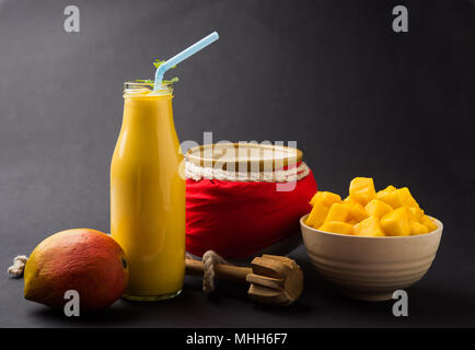 Mango Lassi oder Smoothie in großen Glas oder kleine Flaschen mit Quark, Obst Stücke schneiden und Mixer. Moody Hintergrund, selektiver Fokus Stockfoto