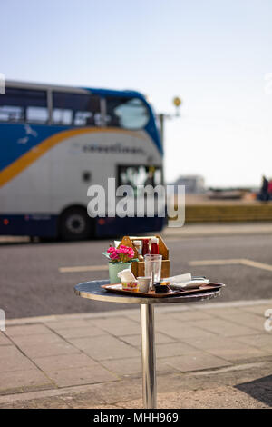 Einen Topf mit Blumen auf einem Cafe Tabelle mit Menschen in Worthing, West Sussex, England Stockfoto