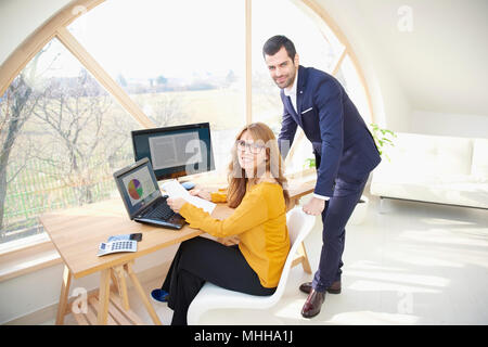 Happy Geschäftsfrau Arbeiten am Laptop während Junge finanzielle Geschäftsmann stand neben ihr und gemeinsam mit dem Finanzbericht. Teamarbeit bei der Stockfoto
